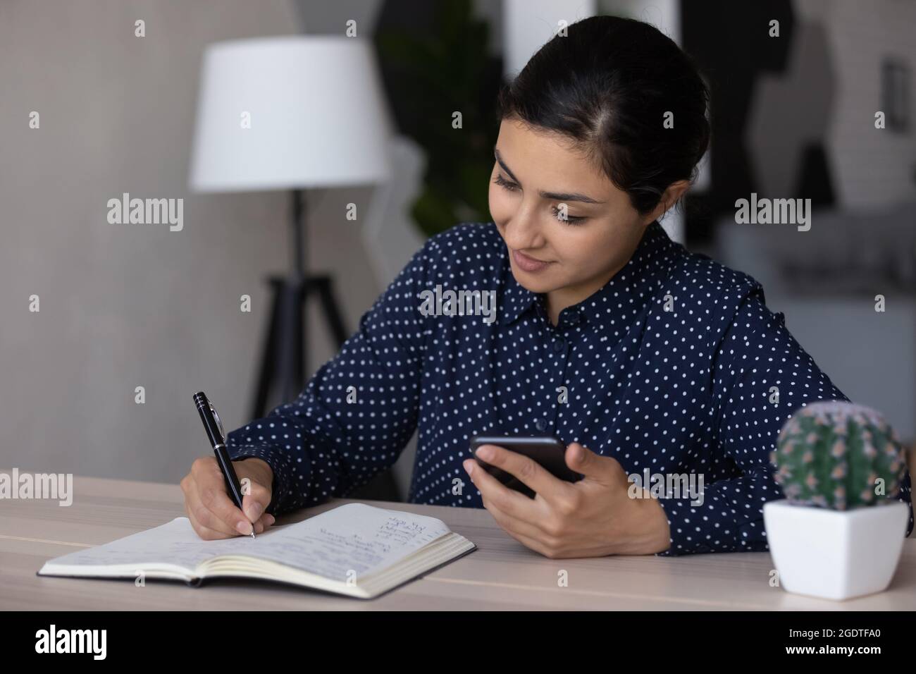 Junge indische Frau schreiben in Notizblock verwenden Handy Stockfoto