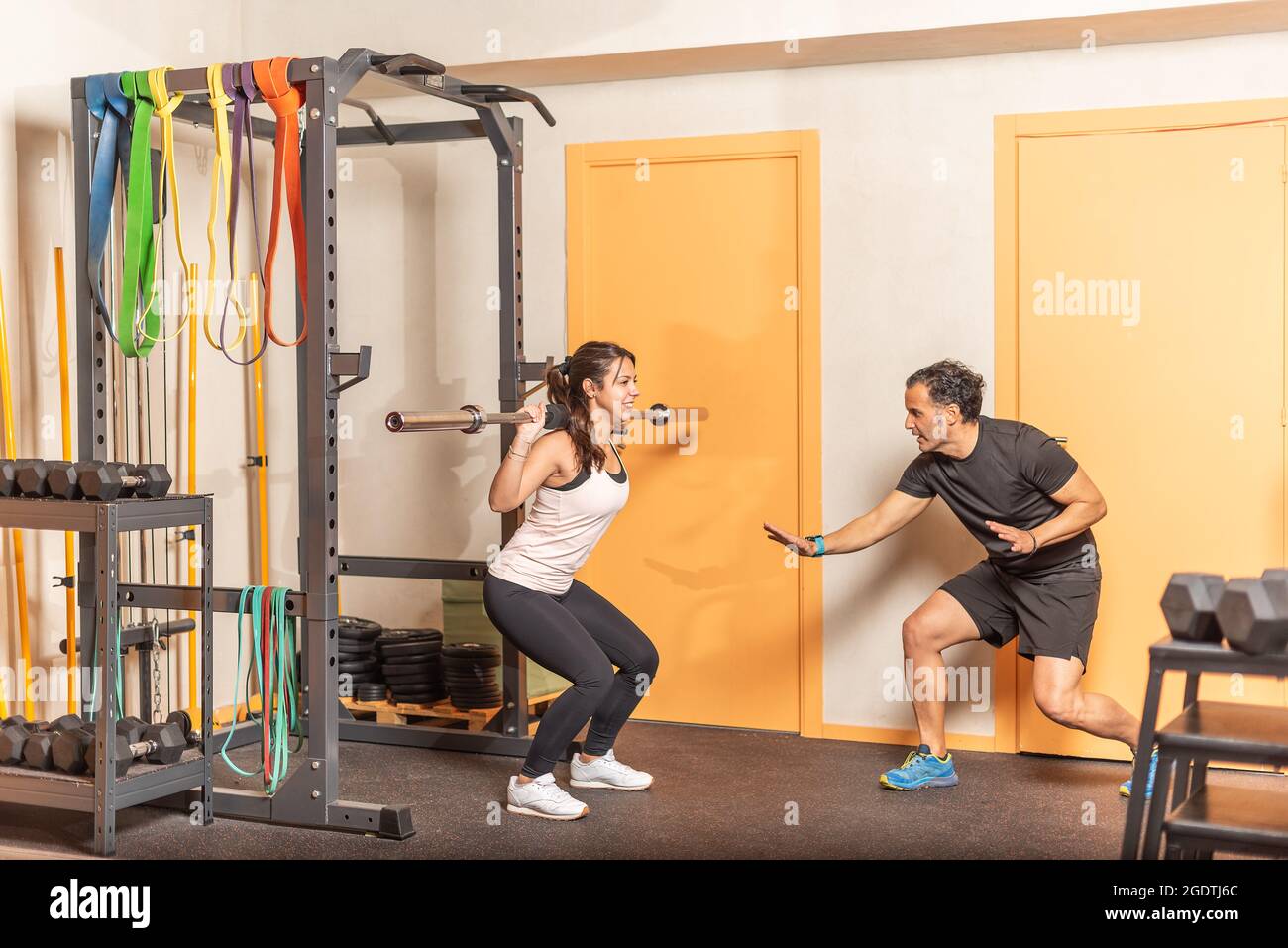 Die Sportlerin hockt mit der Bar und dem Trainer im Fitnessstudio Stockfoto