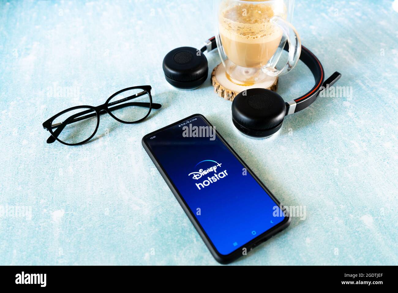 Handy-Smartphone mit beliebter OTT-Streaming-App hotstar Disney plus in Indien. Flatlay-Aufnahme mit Kopfhörerspezifikationen und einer Tasse Kaffee Stockfoto