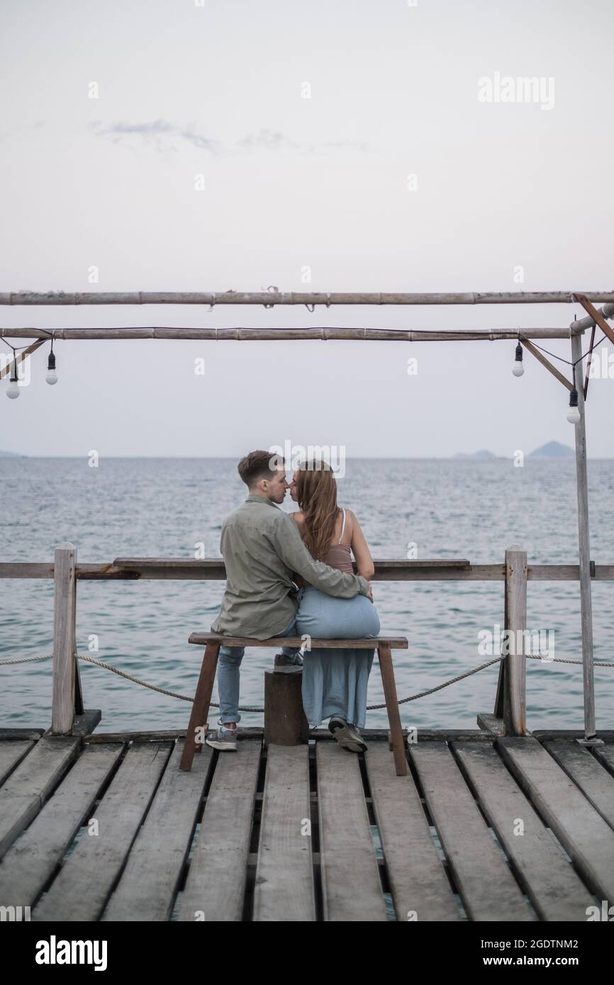 Schönes Paar, das auf der Holzbank am Pier sitzt. Küssen und Kuscheln. Millennials. Romantisches Bild. Hochwertige Fotos Stockfoto