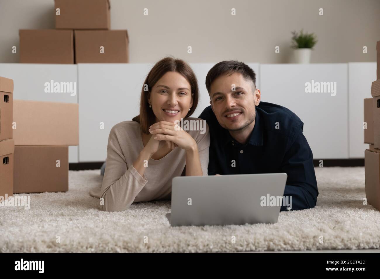 Entspanntes Paar, das mit einem Laptop auf dem Boden liegt, Pappkartons in der Nähe Stockfoto