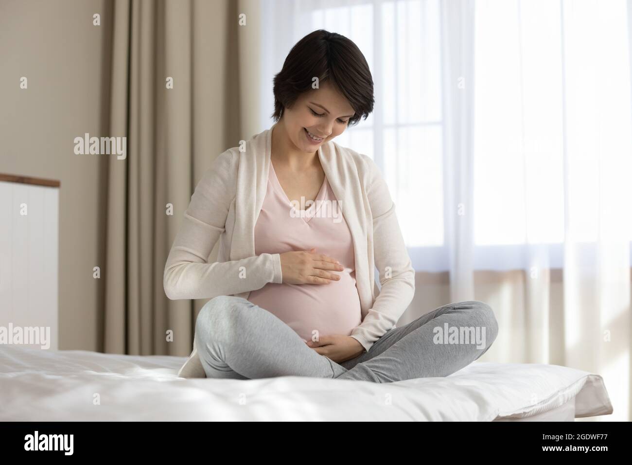 Glücklich junge werdende Mutter auf dem Bett sitzend, streicheln großen Bauch Stockfoto
