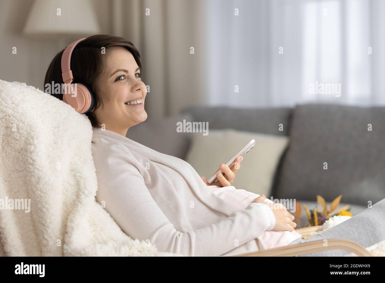 Lächelnde Schwangerin in kabellosen Kopfhörern, die Musik hören Stockfoto