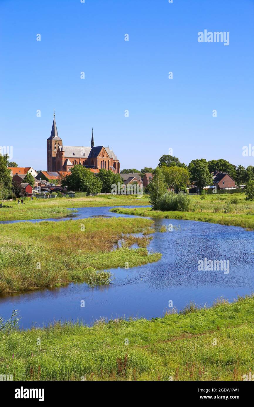 Blick über grünes Feuchtwasser auf das Stadtbild der Stadt durch mit Turm einer mittelalterlichen Kirche gegen blauen Sommerhimmel - Neer (Limburg), Niederlande Stockfoto