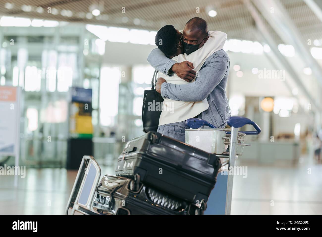 Afrikanisches Paar umarmt sich gegenseitig bei der Ankunft am Flughafen. Junge Männer und Frauen treffen sich während einer Pandemie am Flughafen. Stockfoto