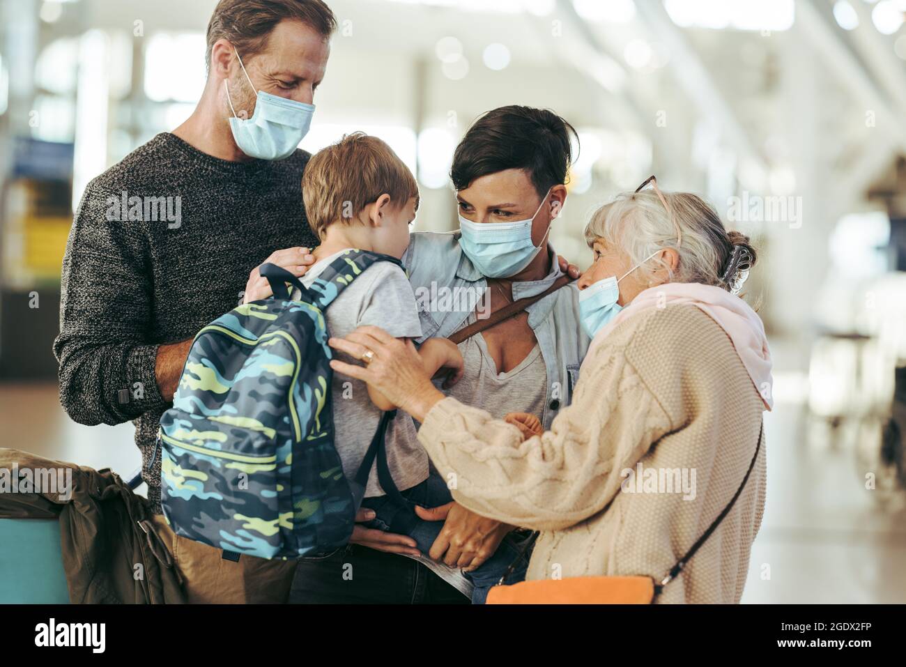 Oma trifft Familie am Flughafen nach langer pandemischer Sperre. Ältere Frau und Familie in Gesichtsmasken bei der Ankunft am Flughafen. Stockfoto