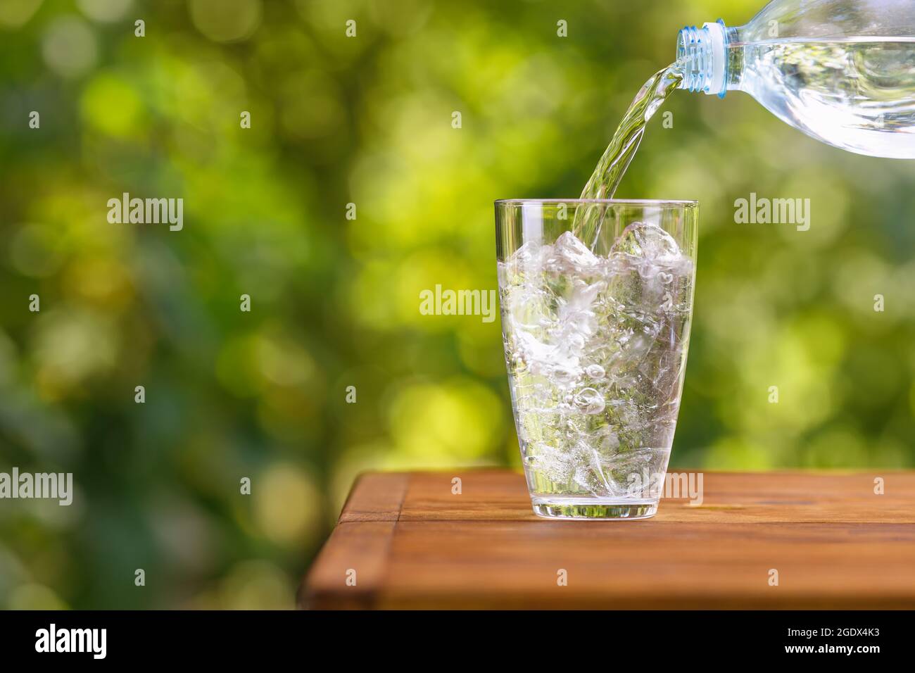 Wasser aus der Plastikflasche, das mit Eiswürfeln in das Glas gegossen wird Stockfoto