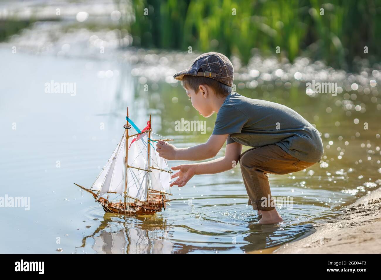 Kleiner Junge in Kappe, der Schiff auf dem Fluss ablauncht Stockfoto