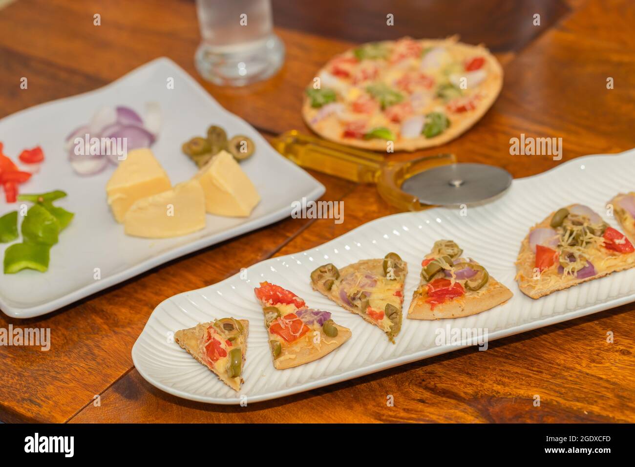 Frisch gebackene und in Scheiben geschnittene Pizza mit Zutaten auf dem Tisch serviert Stockfoto