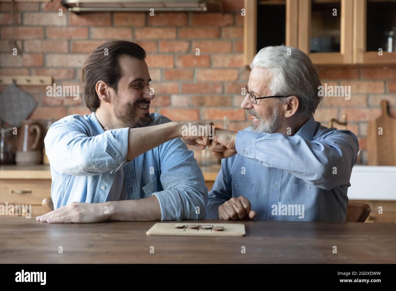 Lächelnder erwachsener Sohn und alter Vater spielen Brettspiel Stockfoto