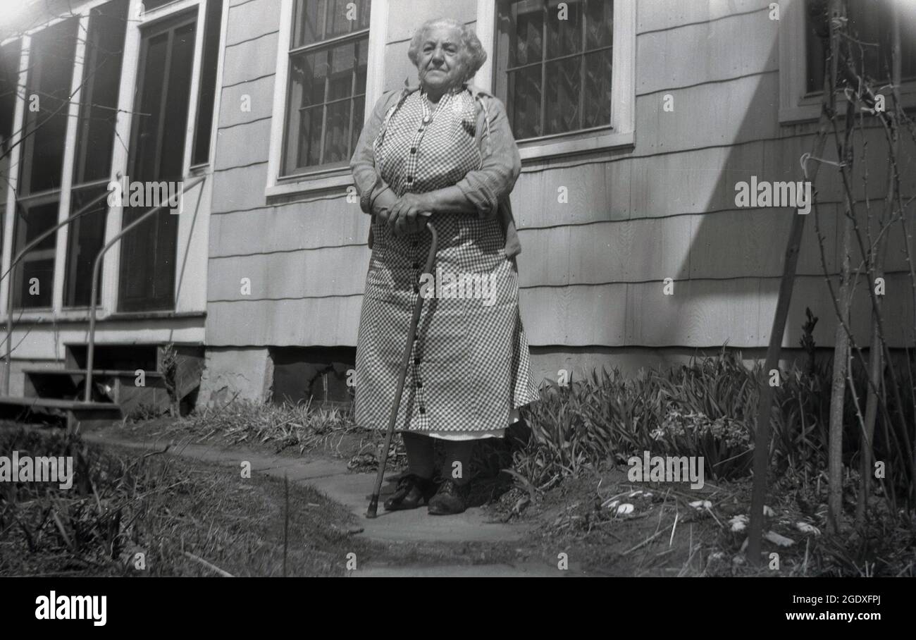 Fünfziger Jahre, historische, ältere Dame, die mit einem Spazierstock vor ihrem Haus stand, des Monies, USA. Stockfoto