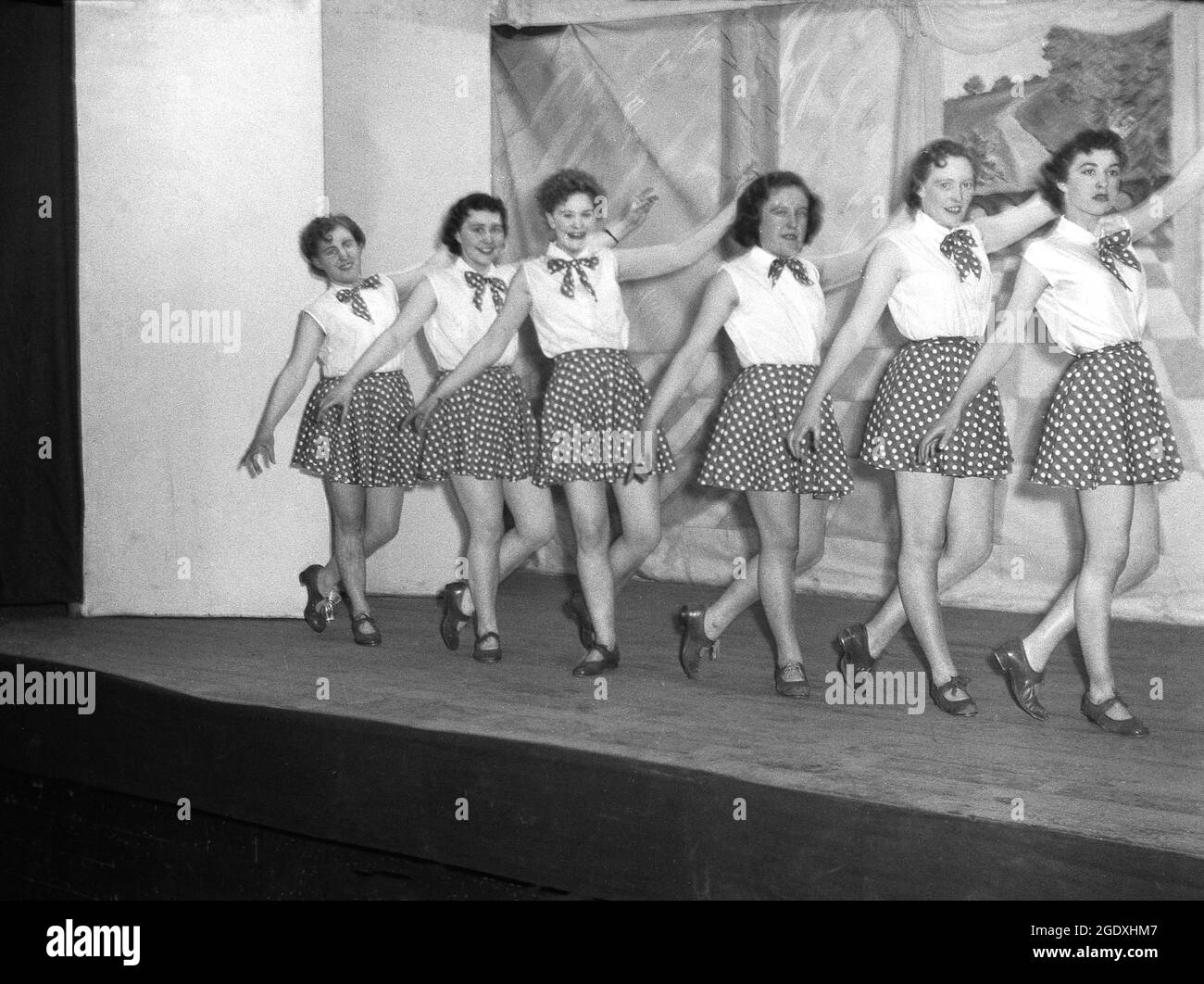 1957, historisch, eine Tanztruppe von Darstellerinnen in ihren Kostümen aus kurzen Röcken mit Punktmuster und ärmellosen Blusen auf der Bühne, die in der Pantomine Aladdin, einer populären Geschichte, die auf einer mittelöstlichen Volksgeschichte basiert, England, Großbritannien, auftaucht. Stockfoto