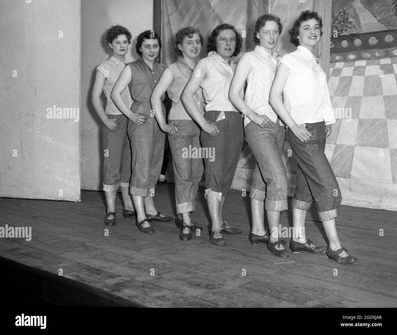 1957, historische, junge weibliche Performer in ihren Kostümen - Jeans, die unter dem Knie aufgedreht wurden und ärmellose Blusen - erscheinen in der Pantomine Aladdin, einer Geschichte, die auf einer mittelöstlichen Volksgeschichte basiert und auf der Bühne für ihr Foto steht, England, Großbritannien. Jeans mit Handschellen oder aufgerollten Hosen wurden in Großbritannien zu Beginn des Rock and Roll modisch, als Rockabilly populär wurde. Stockfoto