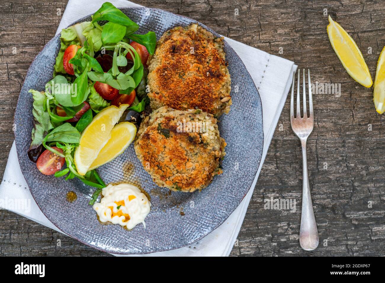 Sardinen-Fischkuchen mit grünem Blattsalat, Knoblauch-Mayo und Zitronenscheiben Stockfoto