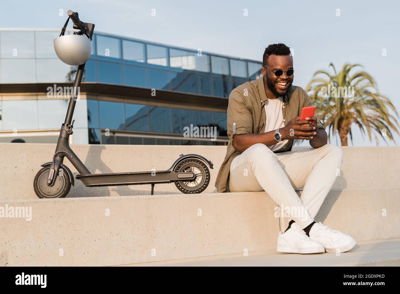 Business african american Mann mit Spaß mit Handy mit Elektroroller im Freien in der Stadt - Fokus auf Gesicht Stockfoto