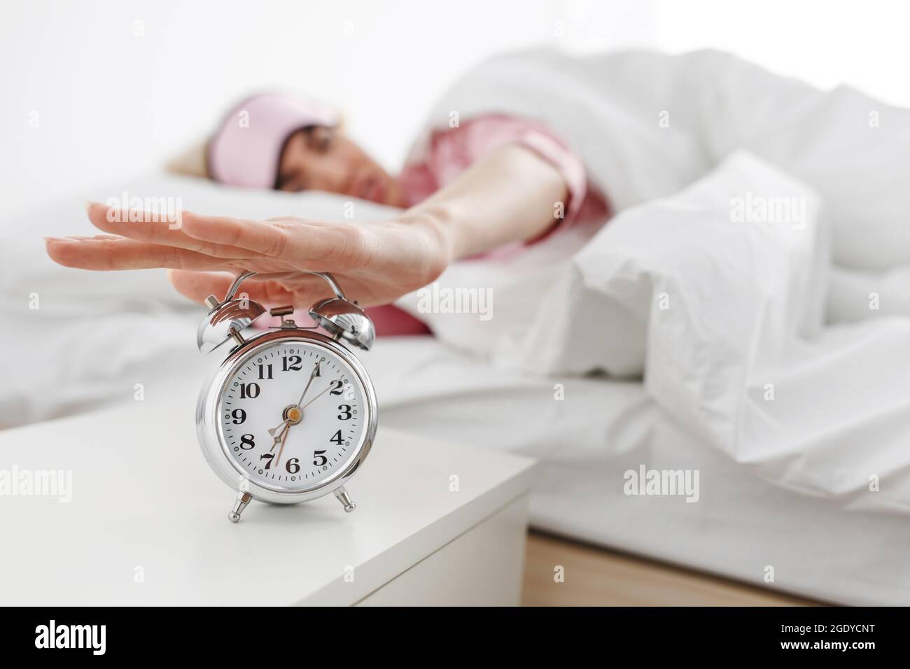 Der Wecker klingelt, die Frau wacht am frühen Morgen zur Arbeit auf, Schlafstörungen Stockfoto