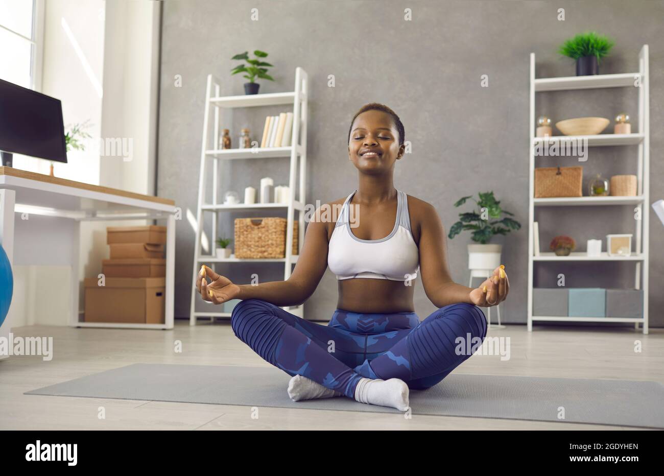 Glückliche schwarze Frau, die zu Hause auf dem Boden sitzt, Yoga praktiziert, sich entspannt und meditiert Stockfoto