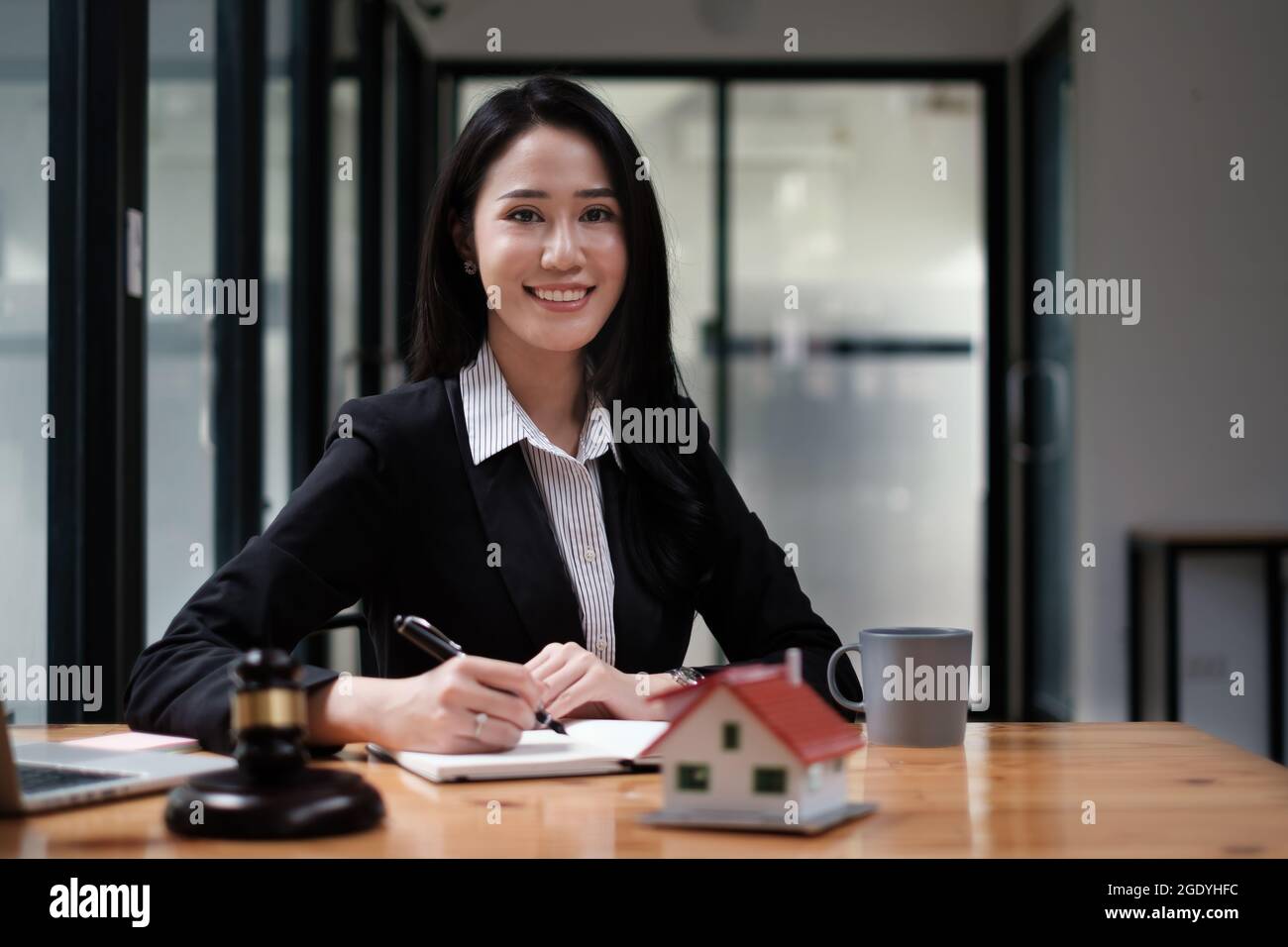 Eine Geschäftsfrau oder Rechtsberaterin sitzt auf einem Holzschreibtisch im Büro. Recht, juristische Dienstleistungen, Beratung, Richter Auktion und Immobilien-Konzept. Stockfoto