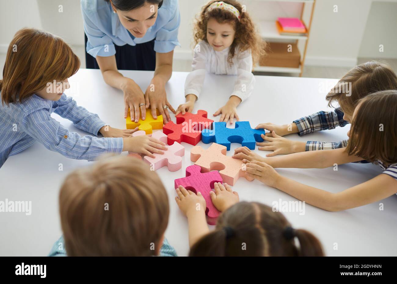 Ein Team von kleinen Schülern mit ihrem Lehrer, das Puzzleteile in einer Lektion zusammenfügt Stockfoto