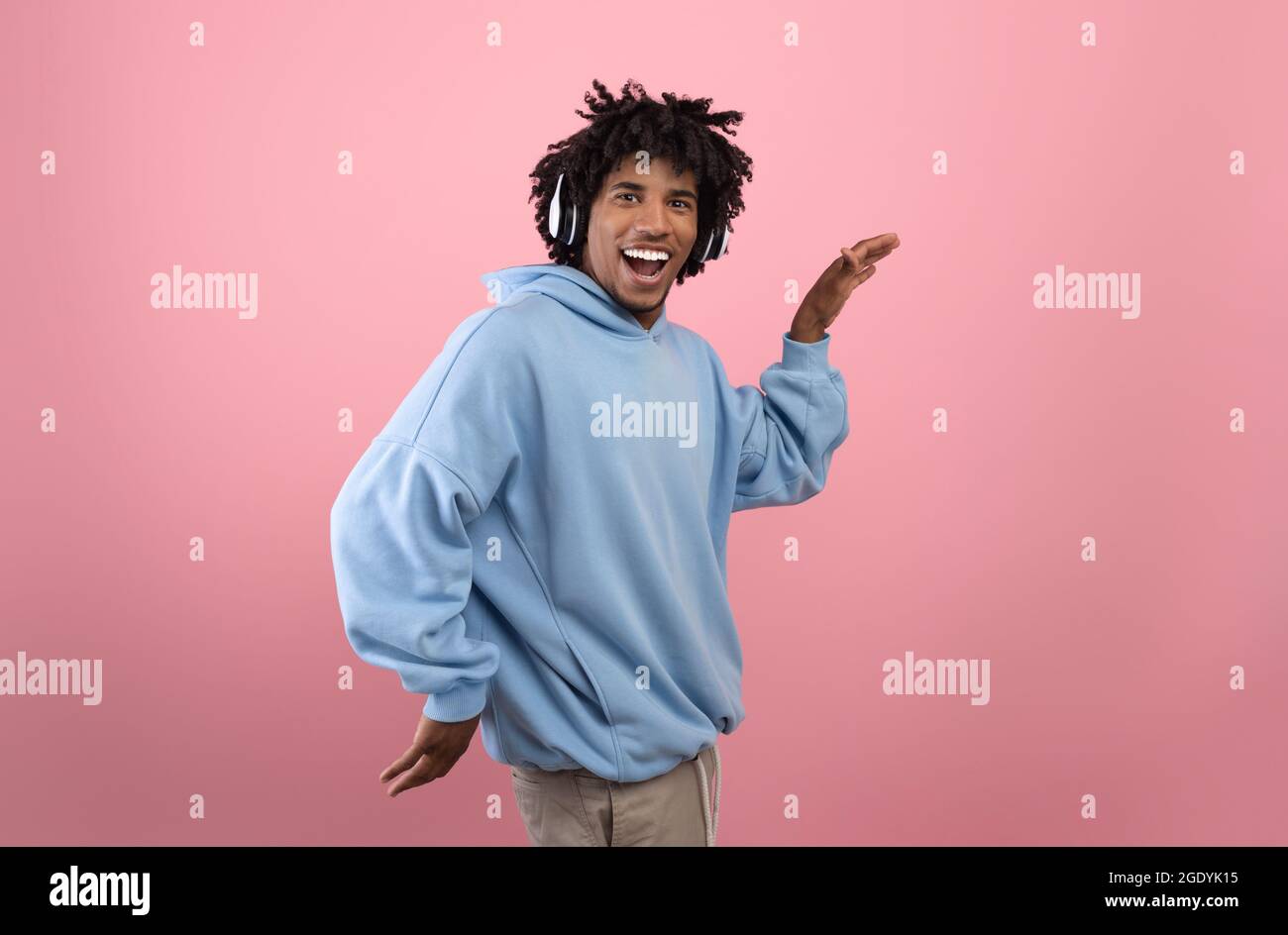 Alberne schwarze Teenager in Kopfhörern, Musik hören, lustigen ägyptischen Tanz tanzen, auf rosa Hintergrund herumtörneln Stockfoto