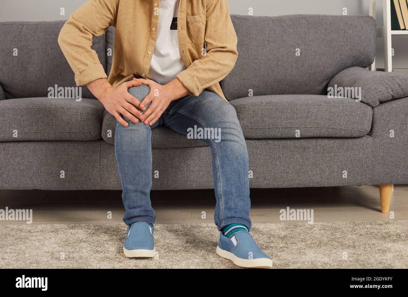 Mann mit Arthritis oder Rheuma sitzt auf dem Sofa und berührt sein schmerzhaftes Knie Stockfoto