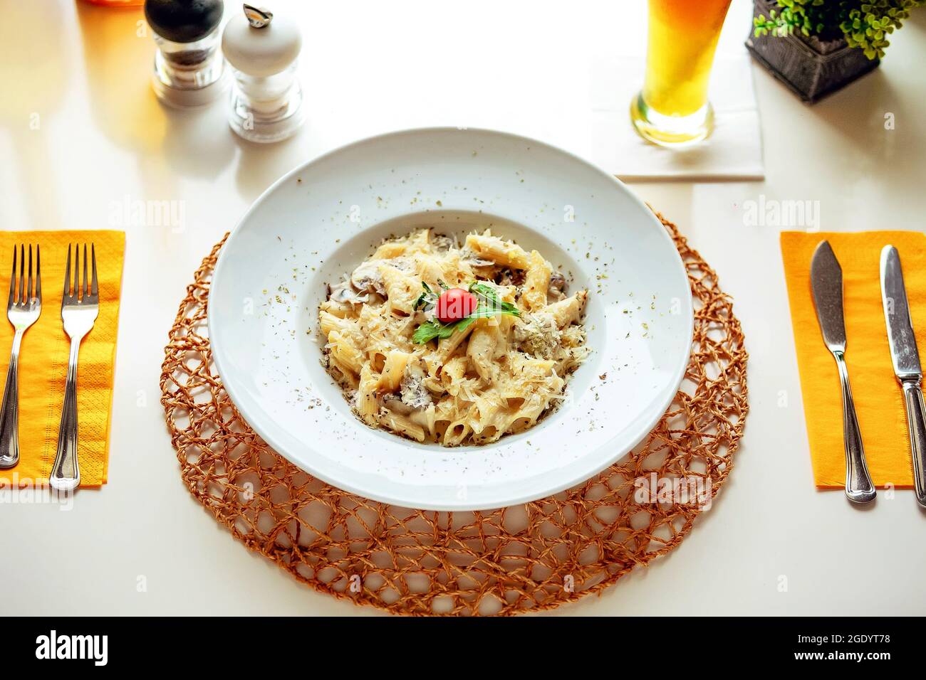 Pasta mit Pilzen in einer weißen Sauce, garniert mit einer Scheibe Kirschtomate und einem Blatt Kräuter Stockfoto