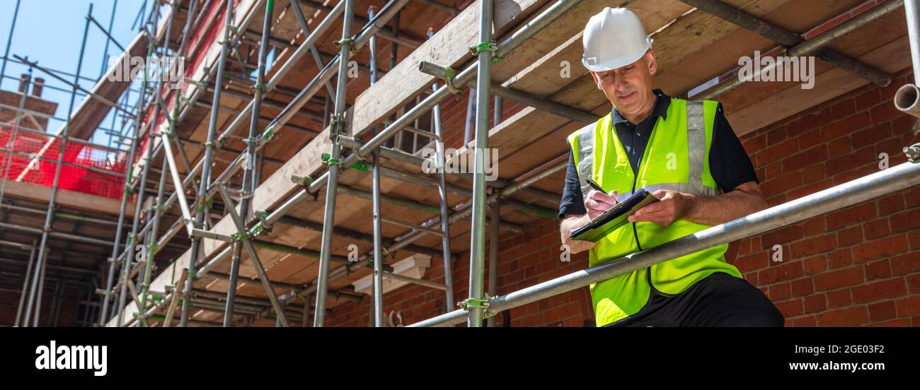 Panorama männlich Baumeister Vorarbeiter, Bauarbeiter, Auftragnehmer oder Architekt auf der Baustelle Schreiben auf schwarzen Zwischenablage Panorama-Web-Banner-Header Stockfoto