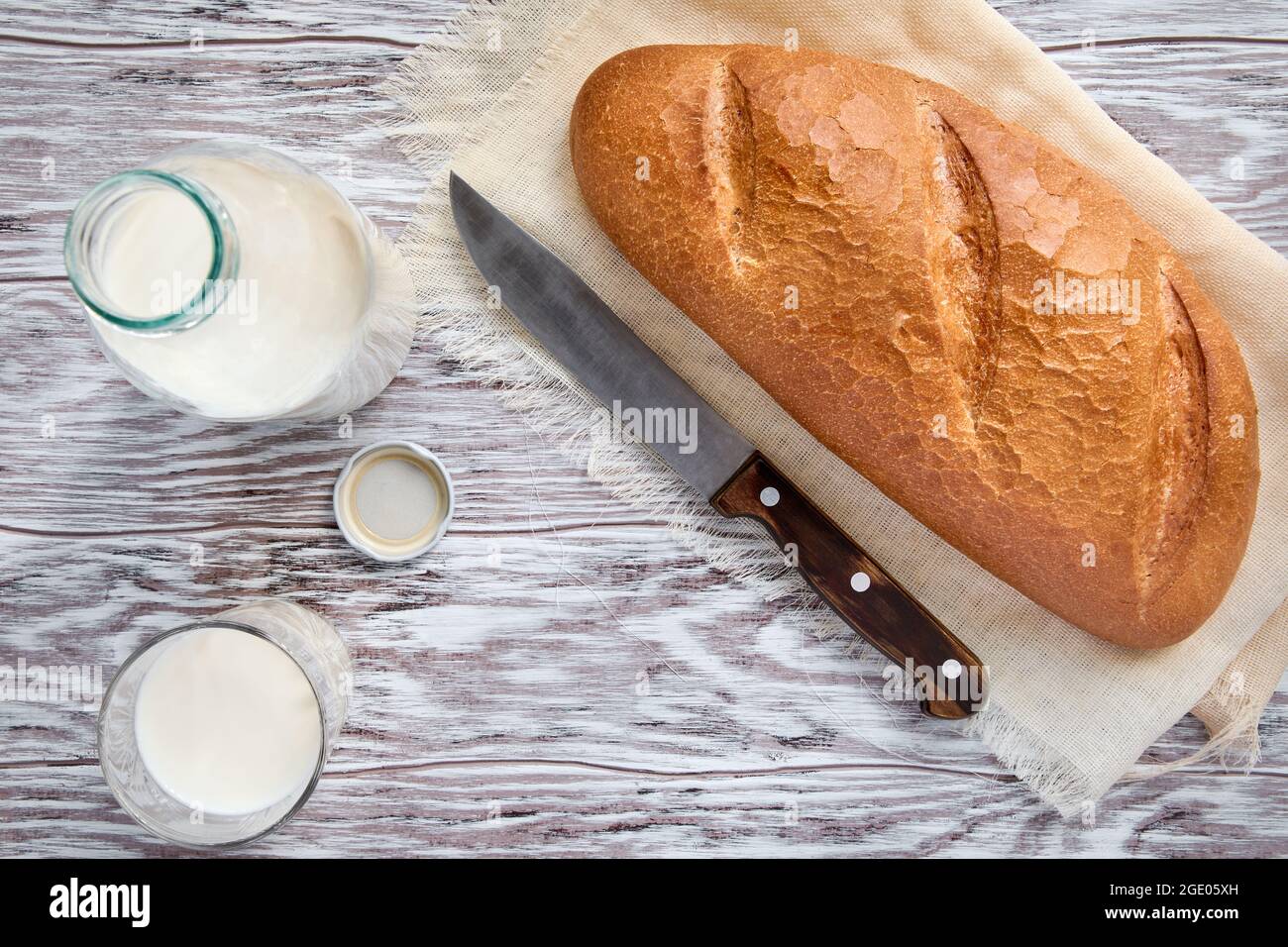 Frische Kuhmilch und ein Laib weißes, warmes, weiches Brot auf einem Holztisch, Draufsicht Stockfoto