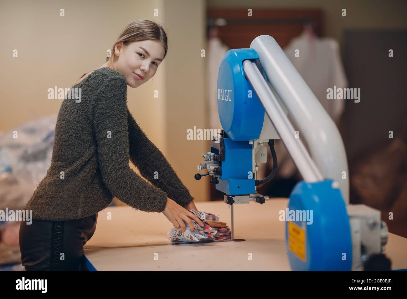 Junge schöne Schneiderin Kleidung Designer schneidet Stoff auf der Maschine. Stockfoto