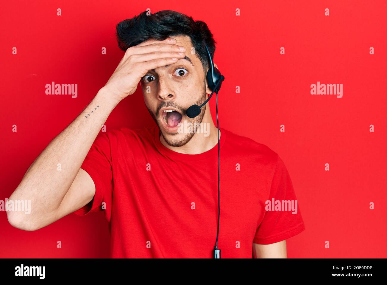 Junger hispanischer Mann mit Headset für Callcenter-Agenten gestresst und frustriert, mit der Hand auf dem Kopf, überrascht und wütend im Gesicht Stockfoto