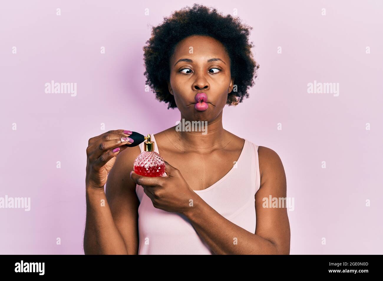 Junge afroamerikanische Frau, die Parfüm hält und Fisch mit Mund und Augen schielt, verrückt und komisch. Stockfoto