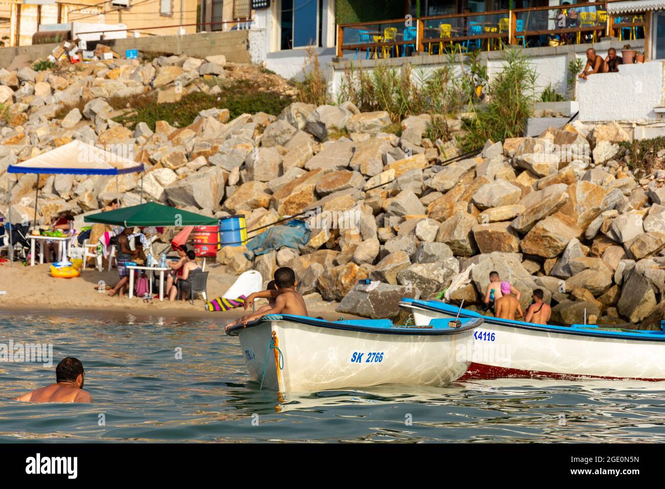 Low-Angle-Ansicht von zwei Kindern in einem Fischerboot und einem Mann im Wasser, Skikda, Algerien. Stockfoto