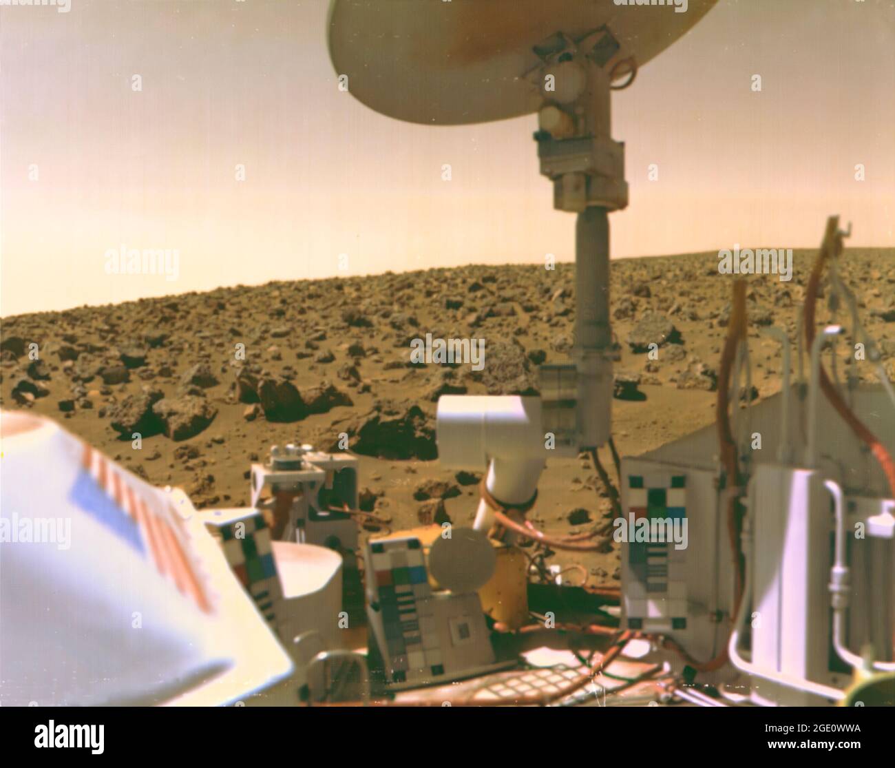Viking 2 Bild der Mars-Utopien-Ebene Beschreibung: Das mit Steinen übersäte Feld aus roten Felsen reicht bis zum Horizont, fast zwei Meilen von Viking 2 auf der Mars-Utopien-Ebene entfernt. Wissenschaftler glauben, dass die Farben der Marsoberfläche und des Himmels auf diesem Foto ihre wahren Farben repräsentieren. Feine Partikel aus rotem Staub haben sich auf den Oberflächen der Raumfahrzeuge niedergelassen. Die Lachsfarbe des Himmels wird durch Staubpartikel verursacht, die in der Atmosphäre schweben. Die Farbkalibrierungstabellen für die Kameras sind an drei Stellen auf dem Raumschiff montiert. Beachten Sie das blaue Sternfeld und die roten Streifen der Flagge. Stockfoto