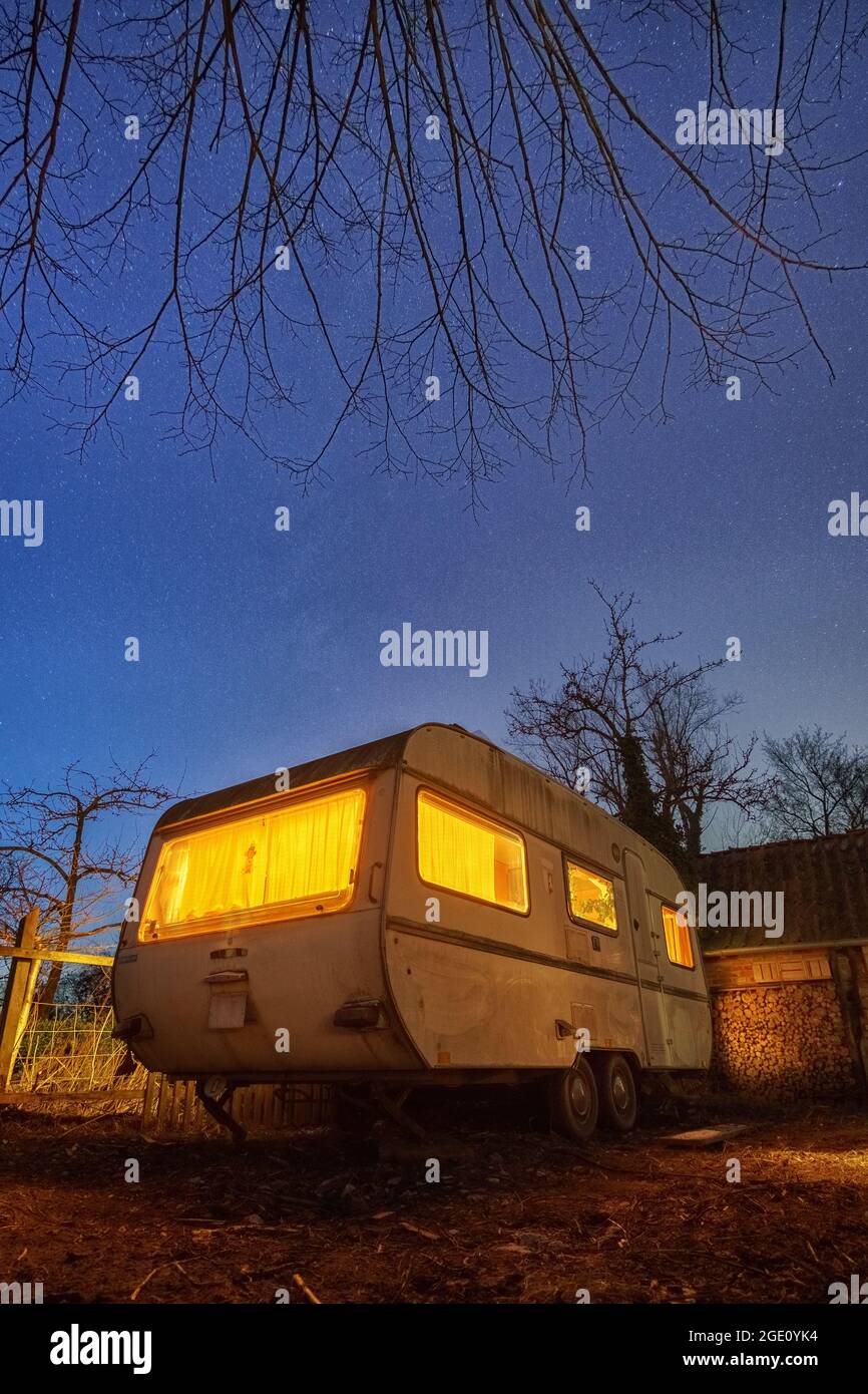 Alter weißer Wohnwagen-Anhänger mit gelber Beleuchtung im Hinterhof bei  stary Blue Night Stockfotografie - Alamy