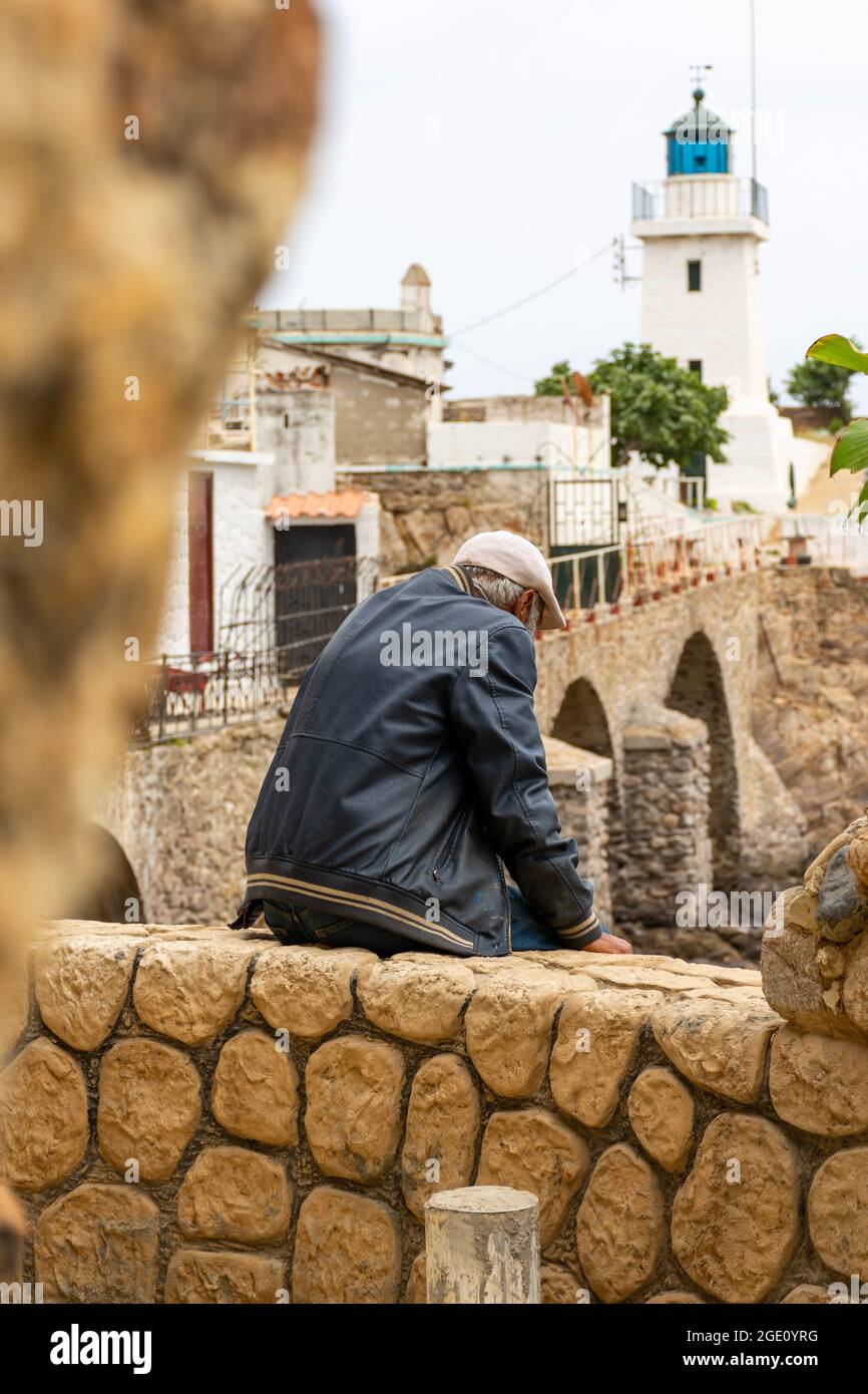 Rückansicht eines mittleren Alters, der auf der Felswand sitzt, eines alten kleinen Leuchtturms. Stockfoto