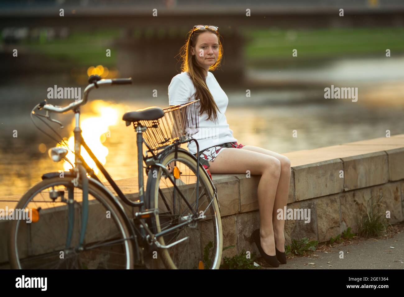 Teenager-Mädchen mit einem Fahrrad auf dem Flussufer während des Sonnenuntergangs. Stockfoto