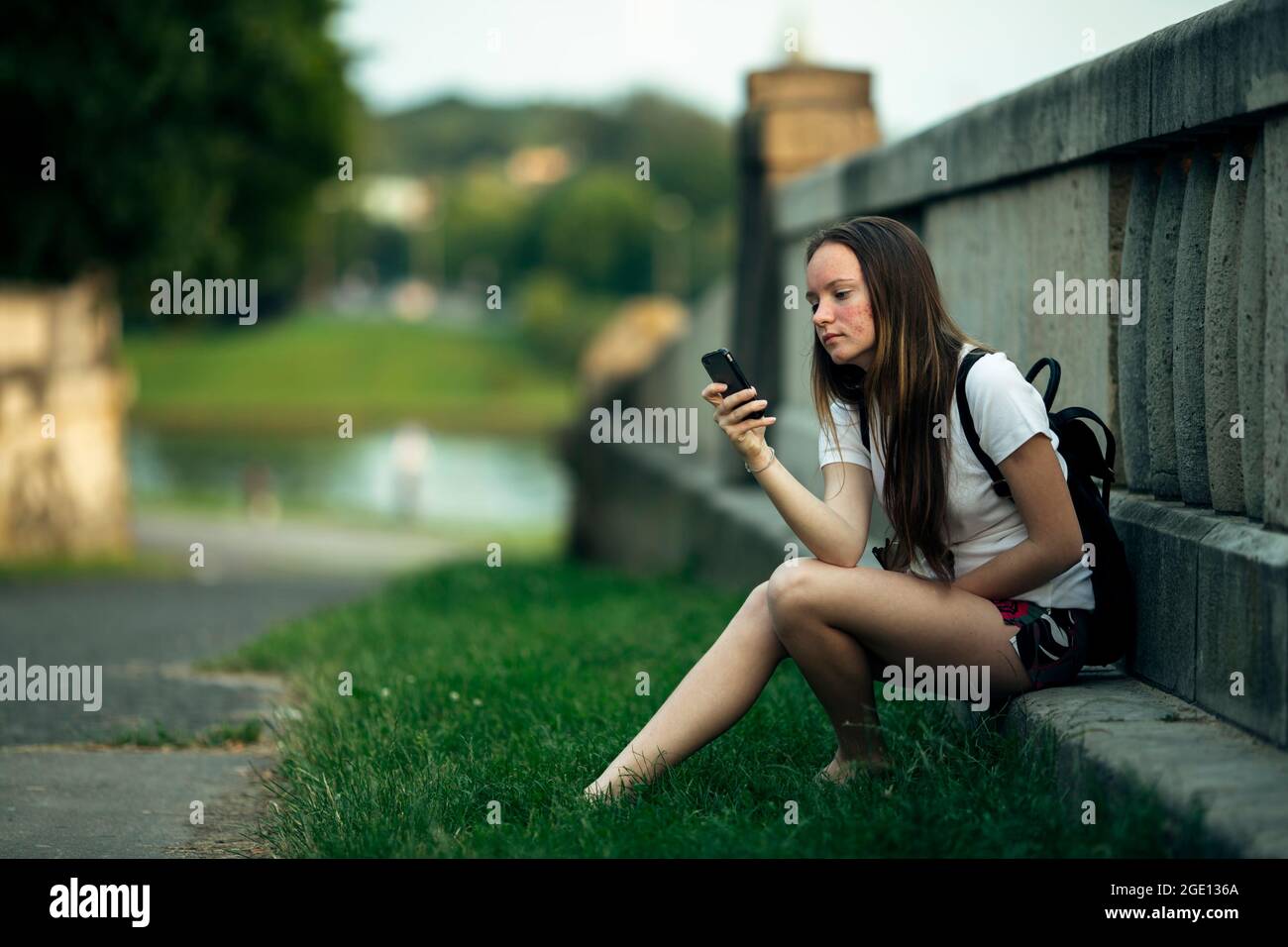 Ein Mädchen im Teenageralter sitzt mit einem Smartphone auf der Straße. Stockfoto