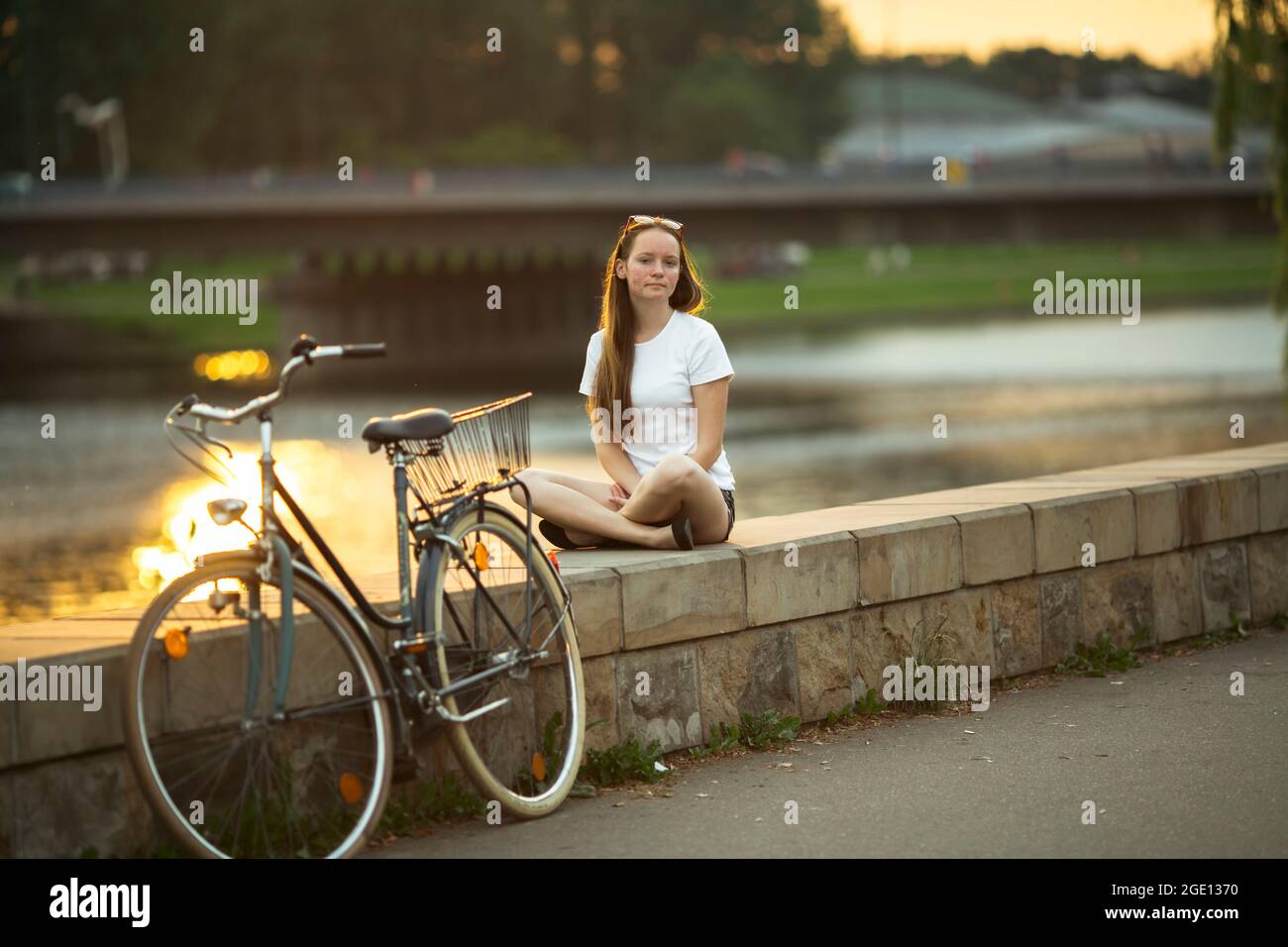 Ein Mädchen im Teenageralter mit einem Fahrrad am Flussufer während des Sonnenuntergangs. Stockfoto