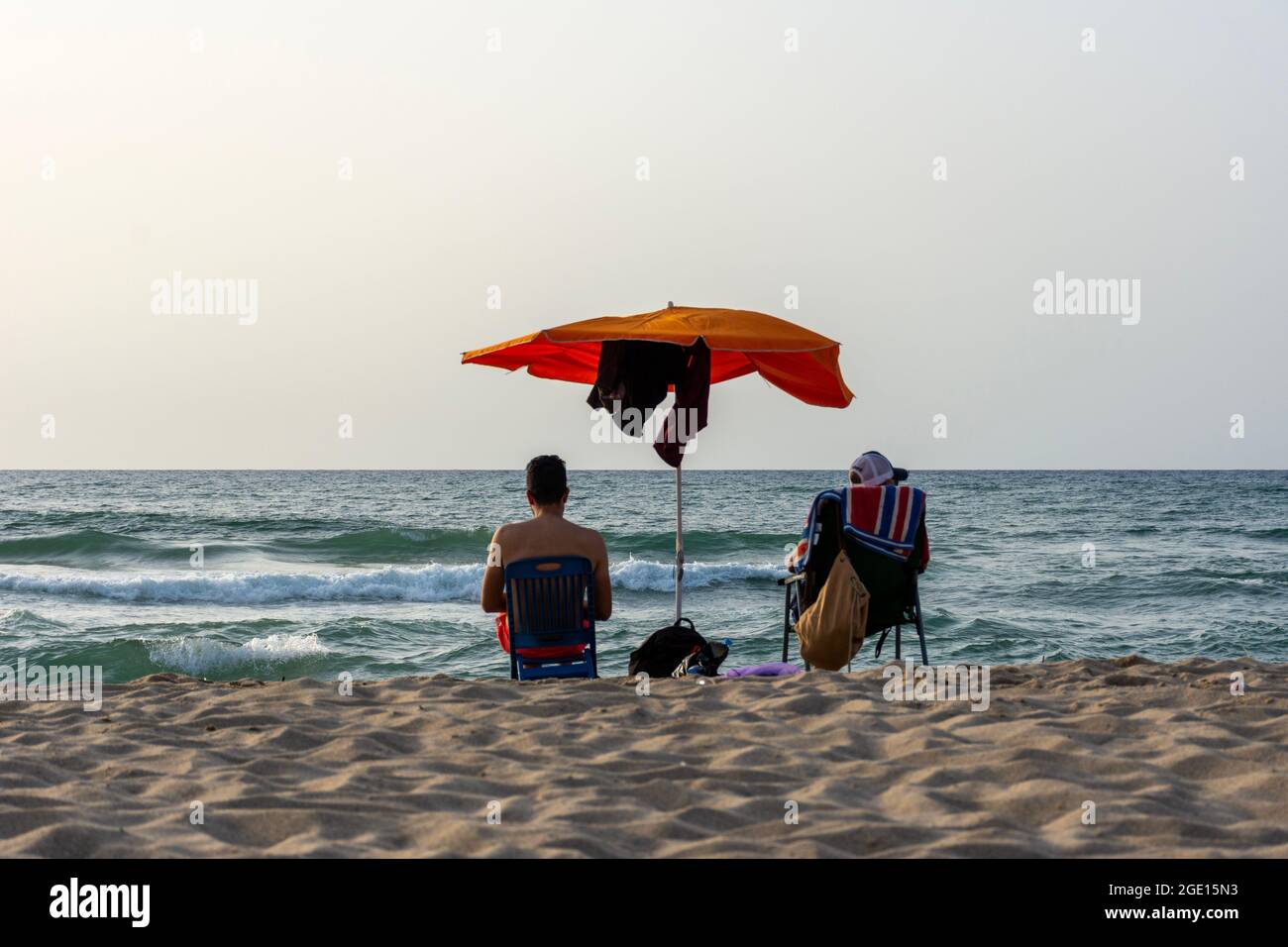 Blick aus der Nähe auf zwei junge Männer, die auf einem Stuhl unter einem Sonnenschirm mit Blick auf das Meer, Skikda, Algerien, sitzen. Stockfoto