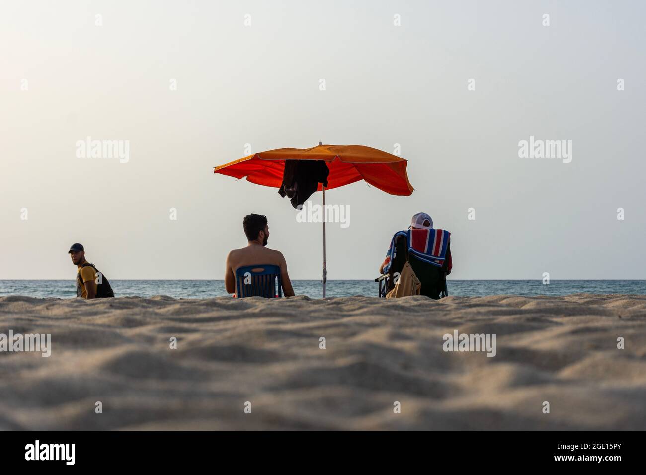 Blick aus der Nähe auf zwei junge Männer, die auf einem Stuhl unter einem Sonnenschirm mit Blick auf das Meer, Skikda, Algerien, sitzen. Stockfoto