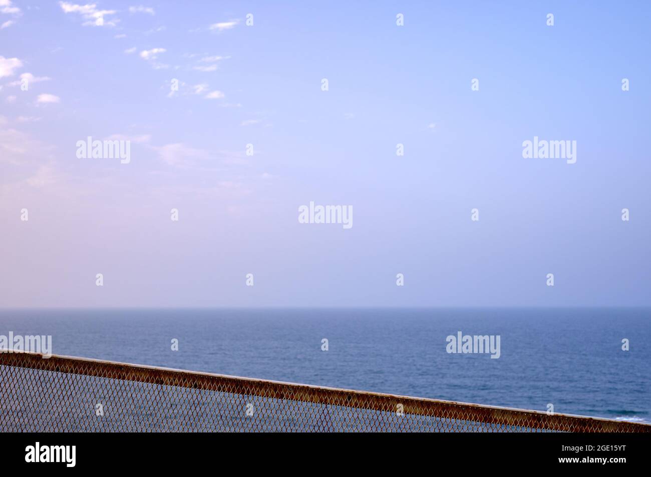 Detail eines verrosteten Metallgeländers mit dem Meer und dem blauen Himmel im Hintergrund Stockfoto