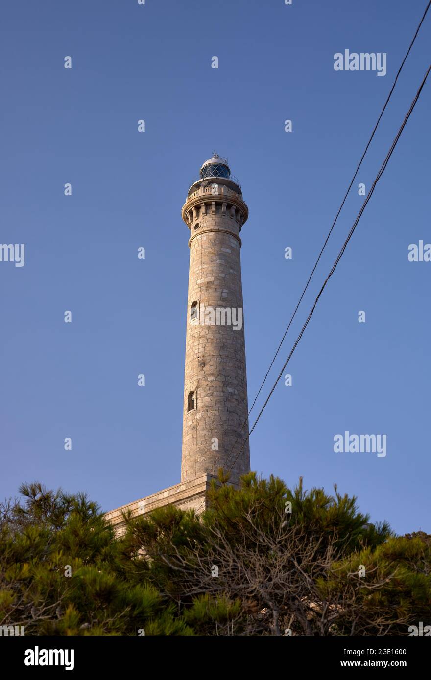 Detail eines steinernen Leuchtturms mit blauem Himmel und Bäumen an seiner Basis Stockfoto