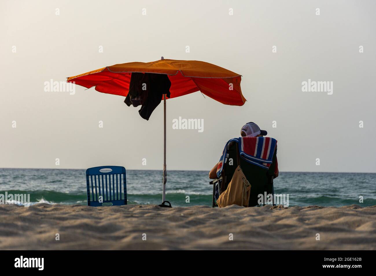 Rückansicht eines jungen Mannes auf einem Stuhl unter einem Sonnenschirm mit Blick auf das Meer, Skikda, Algerien. Stockfoto