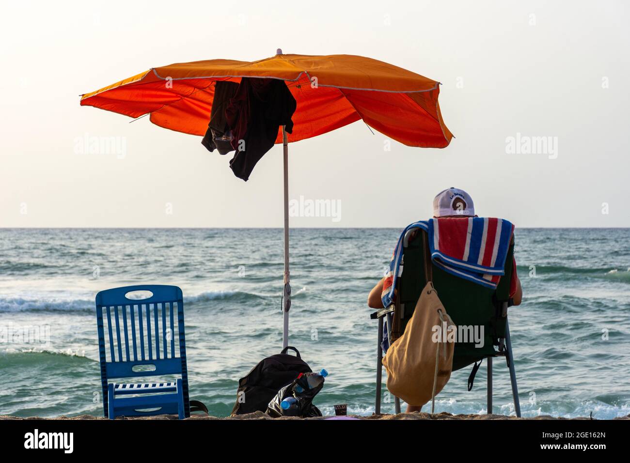 Rückansicht eines jungen Mannes auf einem Stuhl unter einem Sonnenschirm mit Blick auf das Meer, Skikda, Algerien. Stockfoto