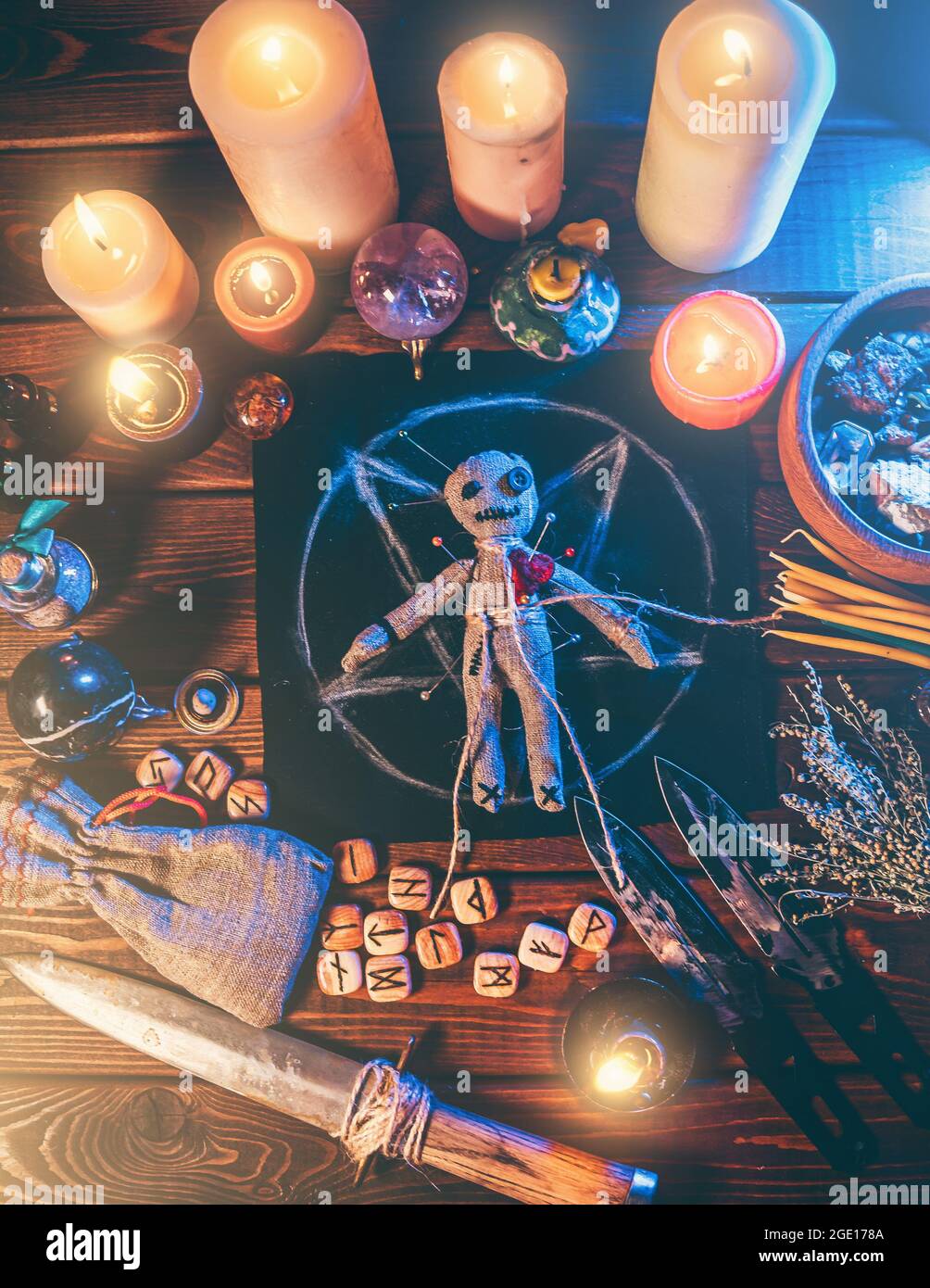 Voodoo-Puppe mit Nadeln in der Mitte des magischen Tisches mit Kerzen und okkulten Objekten Draufsicht besetzt. Magisches und düsteres gruseliges Ritual. Vergeltung oder Rache durch Hexerei-Konzept. Stockfoto