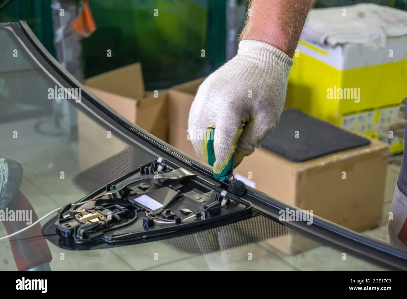 Der Servicemitarbeiter deckt die Kante der Windschutzscheibe mit Klebstoff ab, bevor er sie auf das Auto montiert. Stockfoto