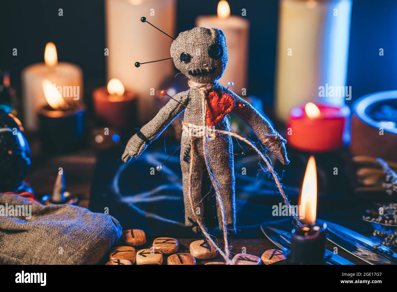 Voodoo Puppe mit Nadeln in magischen Tisch mit Kerzen und okkulten Objekten besetzt. Magisches und düsteres gruseliges Ritual. Vergeltung oder Rache durch Hexerei-Konzept. Stockfoto