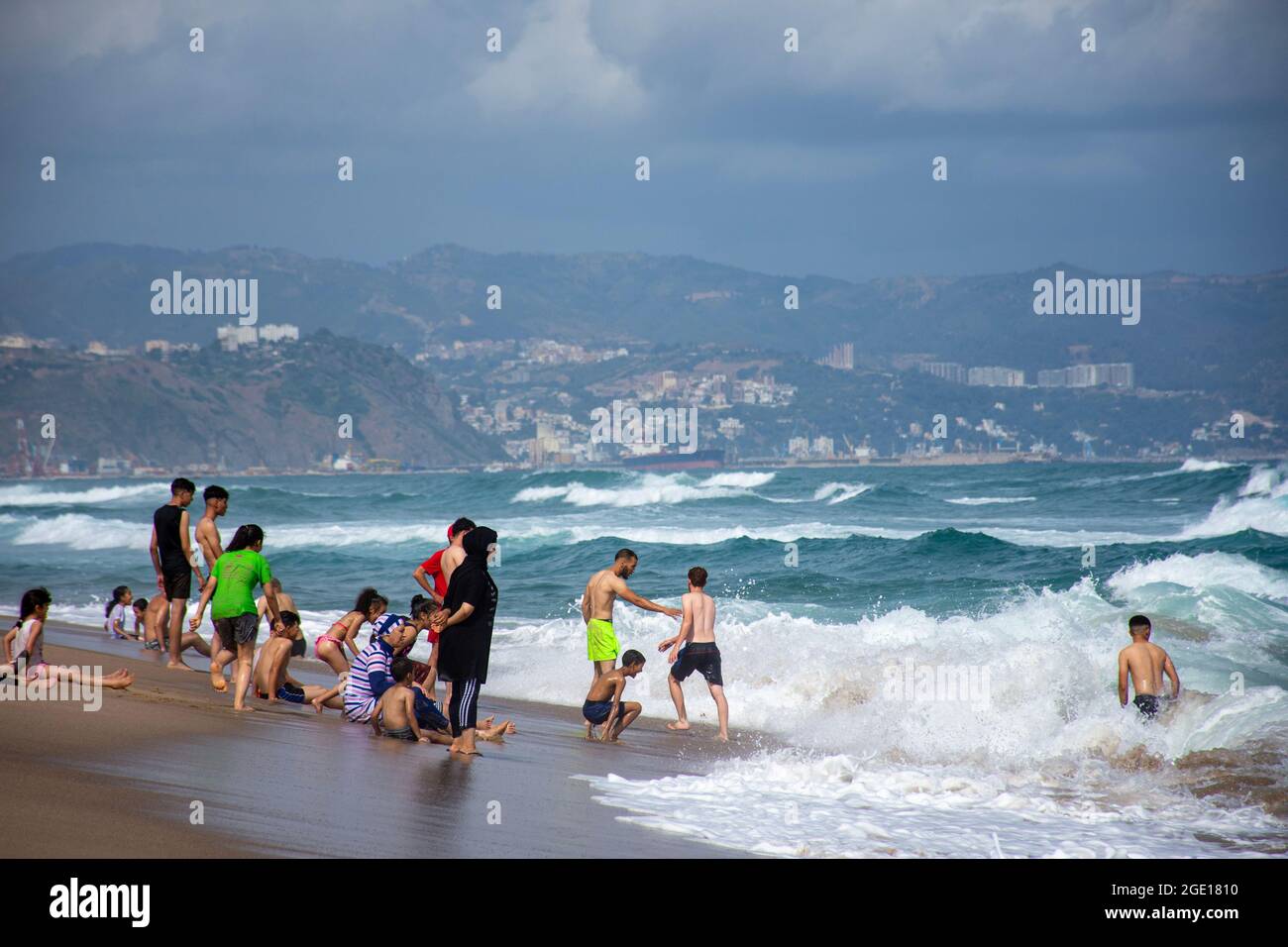 Gruppe von Menschen, die im Meeresschaum am Strand von Jeanne D'Arc, Skikda, Algerien, stehen. Stockfoto