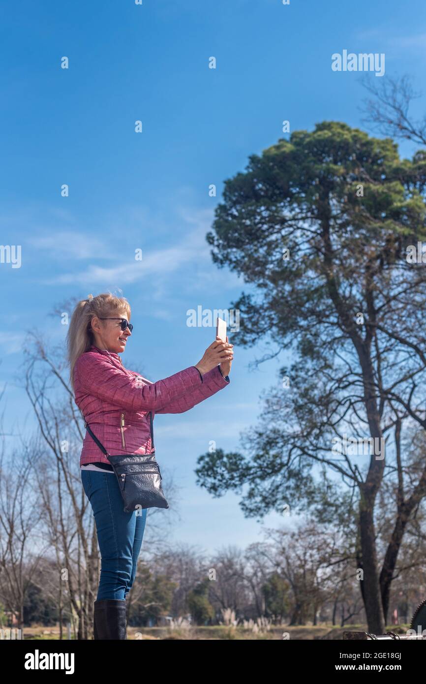 Verkürzte Seitenansicht einer erwachsenen Frau mit Sonnenbrille, die an einem sonnigen Tag ein Foto in einem Park gemacht hat. Stockfoto