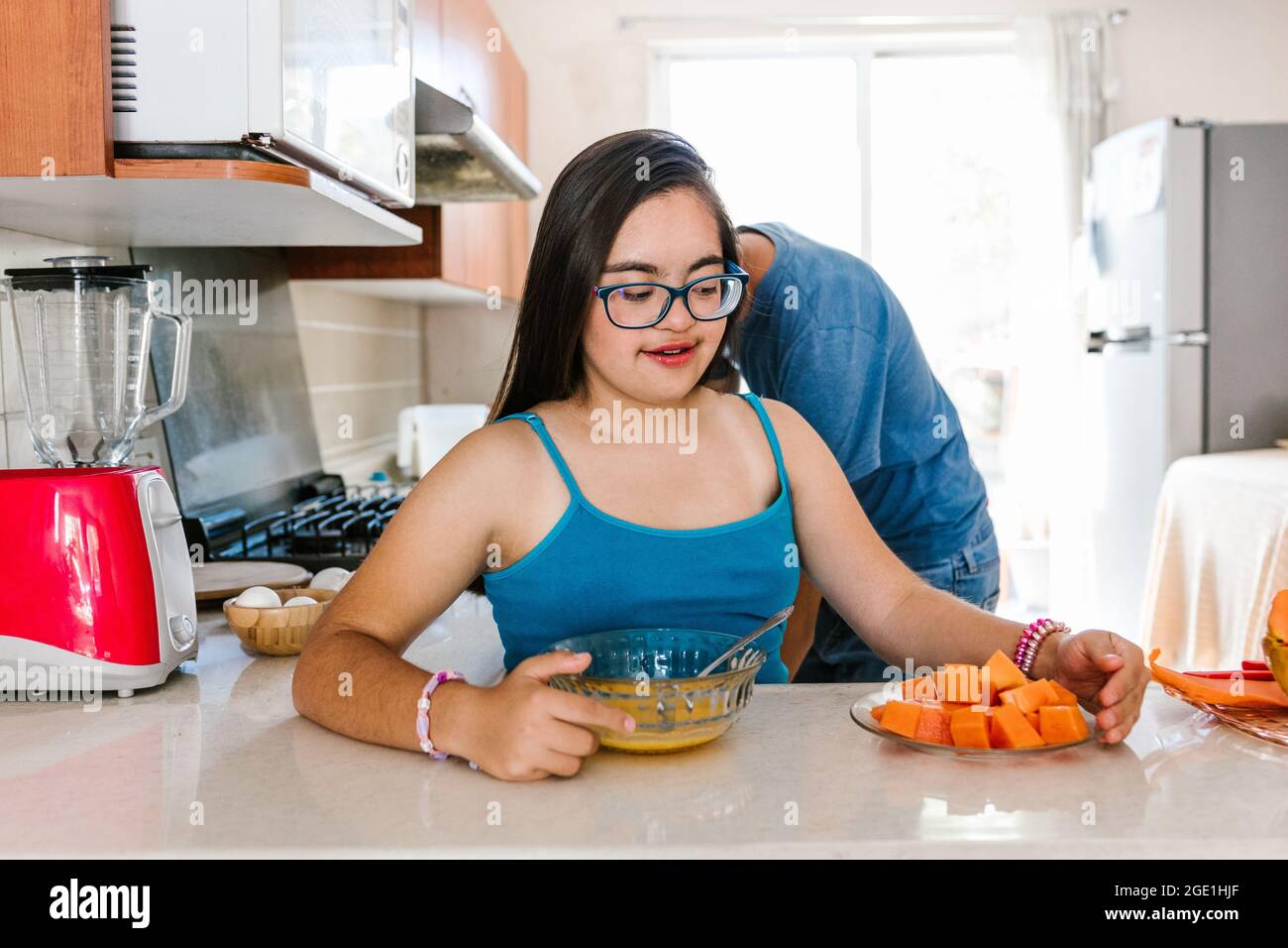 Lateinisches Teenager-Mädchen mit Down-Syndrom, das in der Küche Obst isst, im Behindertenkonzept in Lateinamerika Stockfoto